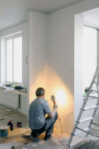 A contractor working on wiring inside a home, using a spotlight to inspect the wall. Ensure your renovation is handled by the right contractor—contact us today!