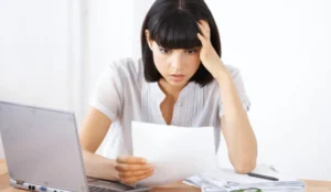 A concerned woman reviewing a document at her desk, with a laptop and bills nearby. Avoid costly remodeling mistakes by getting expert advice today!